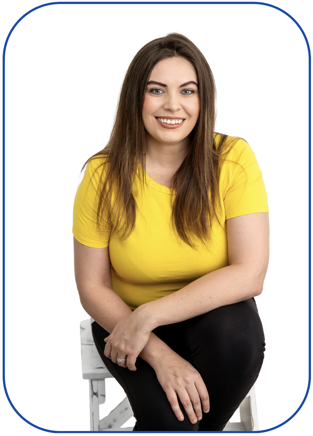 Smiling woman in a yellow shirt seated on a white stool, with long brown hair, against a white background within a blue border frame