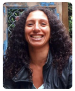 Joyful woman with curly hair smiling in front of a blurred greenery backdrop