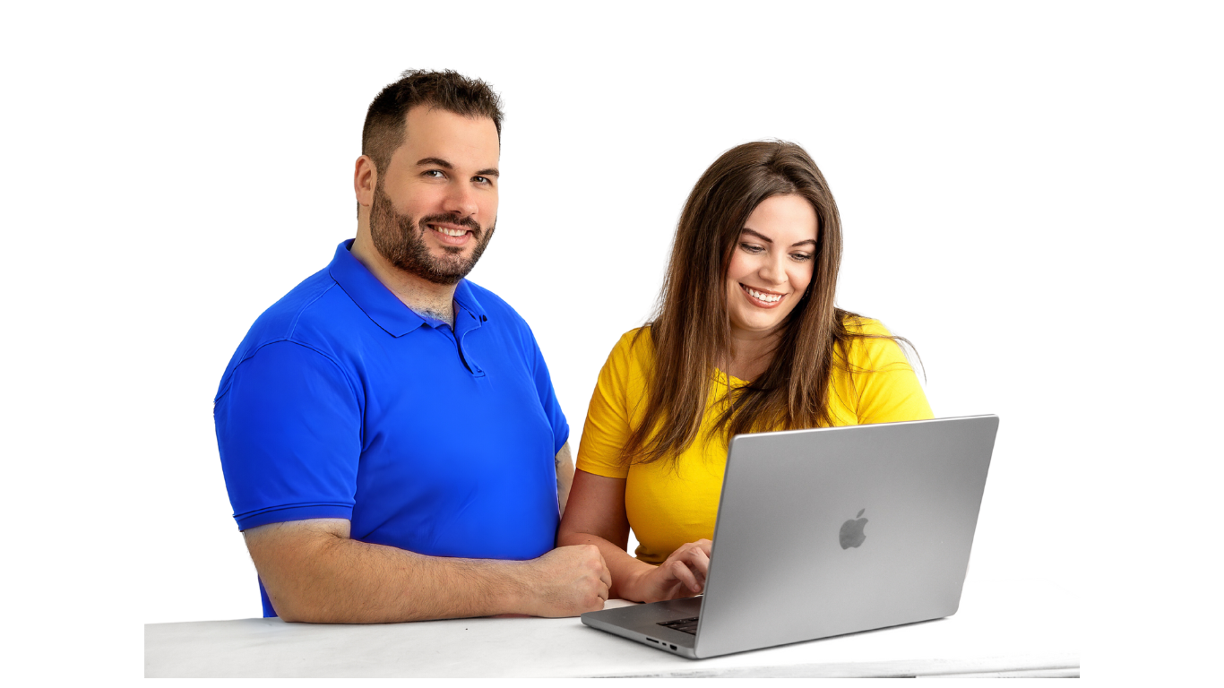 Two smiling people with a man in a blue polo shirt standing behind a seated woman in a yellow top, both looking at a laptop on a table against a white background