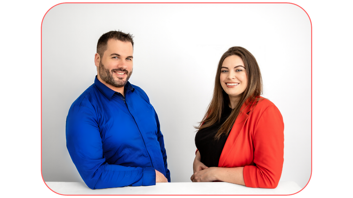 A smiling man in a blue shirt and a woman in a red blazer leaning on a white table, with a white background enclosed by a rounded red border